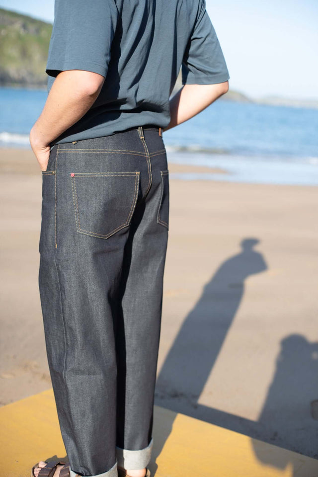 Person wearing dark jeans and a gray shirt on a beach with a clear sky.